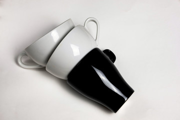 Modern fashionable flat lay, different black and white tea and coffee cups on white background with hard openwork shadows top view. Concept of uniting different colors and shapes, union, acceptance