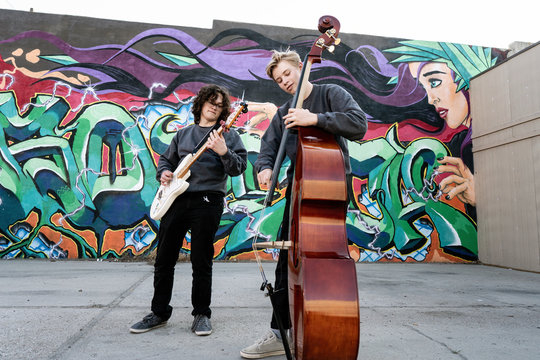 Teenage boys playing bass and guitar by graffiti