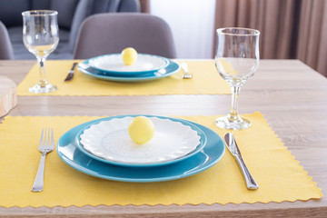 Beautiful Easter Table Setting With Decorations. Blue Plates On Yellow Feeding Mats. Yellow Easter Painted Eggs