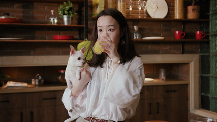 Footage of attractive young woman with nice dog. Girl drinking orange juice. Tasting bad. Indoors. Kitchen. Healthy lifestyle. Food.