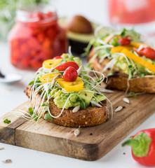 A front facing view of avocado toast garnished with Peruvian peppers, surrounded by the ingredients to make the toast.