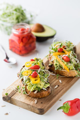 Two pieces of avocado toast garnished with Peruvian drop peppers and a jar of the peppers in behind.