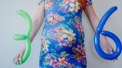 A close up photo of a pregnant young woman holding in her hands the week number thirty six (36)...