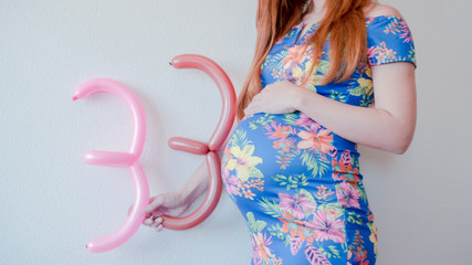 A close up photo of a pregnant young woman holding in her hands the week number thirty three (33)...