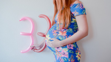 A close up photo of a pregnant young woman holding in her hands the week number thirty three (33)...
