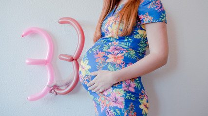 A close up photo of a pregnant young woman holding in her hands the week number thirty three (33)...