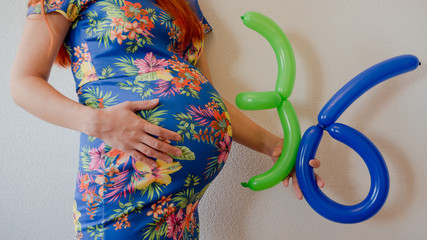 A close up photo of a pregnant young woman holding in her hands the week number thirty six (36)...