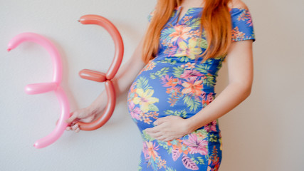 A close up photo of a pregnant young woman holding in her hands the week number thirty three (33)...
