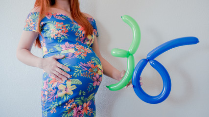 A close up photo of a pregnant young woman holding in her hands the week number thirty six (36)...