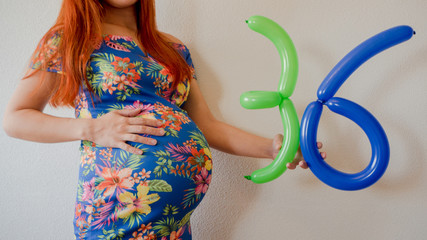 A close up photo of a pregnant young woman holding in her hands the week number thirty six (36)...