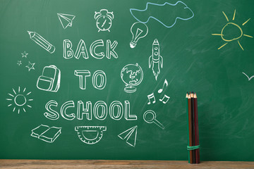 Pencils on table near blackboard with drawings and text BACK TO SCHOOL