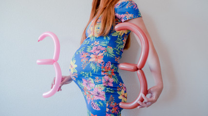A close up photo of a pregnant young woman holding in her hands the week number thirty three (33)...