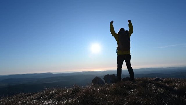 Handheld shot of a female hiker raising hands in victory as she reaches the mountain top