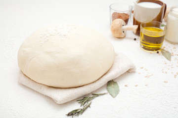 Dough on a white background, sprinkled with flour, decorated with spices, black pepper peas, olive oil, Bay leaf and mushrooms. Concept ingredients for baking or making dough.