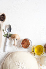 Dough on a white background, sprinkled with flour, decorated with spices, black pepper peas, olive oil, Bay leaf and mushrooms, with copy space. Concept ingredients for baking or making dough.