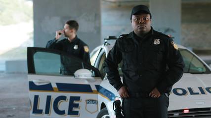Close up african american young man cops stand near patrol car look around background his colleague enforcement happy officer police uniform auto safety security communication control policeman close