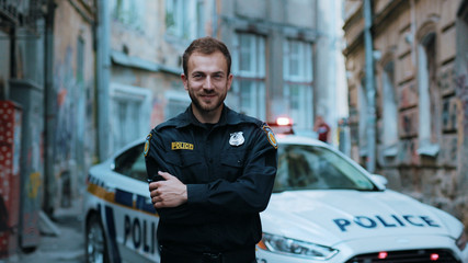 Smiling young man cops stand near patrol car look at camera wear glasses enforcement happy officer police uniform auto safety security communication control policeman close up slow motion