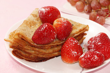 Pancakes with strawberries on a pink sunny background. The concept of healthy and natural food. Healthy breakfast, food for children. selective focus. Traditional Russian pancakes and Shrovetide
