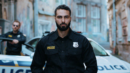 Portrait serious young man cops hold pistol stand near patrol car look at camera enforcement officer police uniform auto safety security communication control policeman portrait close up slow motion