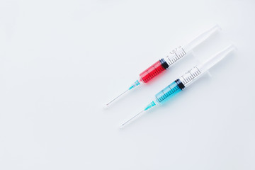 Two syringes filled with blue and red liquids on white background