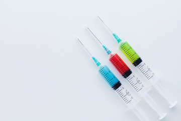 Three syringes filled with blue, red and green liquids on white background
