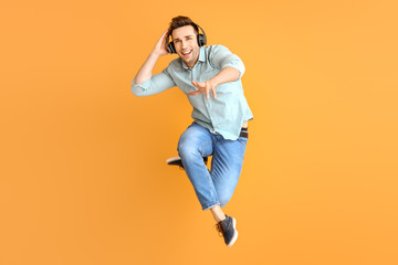 Fototapeta na wymiar Cool jumping young man listening to music against color background