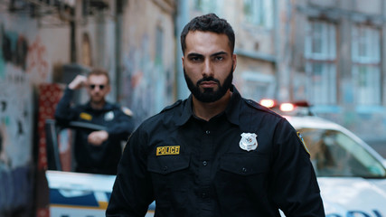 Face young man cops stand near patrol car look at camera serious enforcement officer police uniform auto safety security communication control policeman close up slow motion