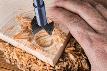 Forstner drill bit detail. Craftsman boring cylindric hole into wood. Hand of joiner on wooden...