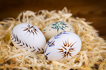 Three ornate Easter eggs in nest of wood shavings on blur background. Casual patterned empty...