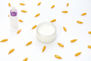 Top view of a white jar of cream, a pink pink glass bottle and golden collagen capsules on a white background. The concept of beauty, facial skin care, cosmetology, medicine