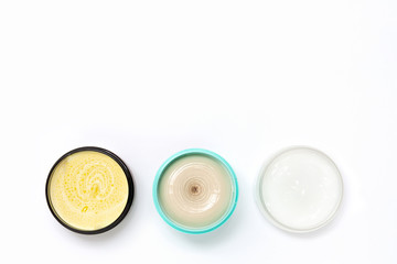 Top view of a black turquoise and white jars with different cream on a white background. The concept of beauty, medicine, facial and body skin care, hair care