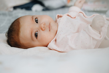 baby girl lying on her back on the bed in a bright bedroom, dressed in a light sundress. calm baby...