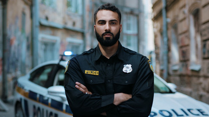 Close up serious young man cops hold pistol stand near patrol car look at camera enforcement officer police uniform auto safety security communication control policeman portrait slow motion