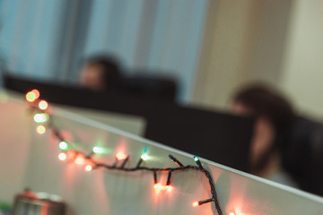 Christmas garland in the IT office. Two blurred programmers sitting at wotk