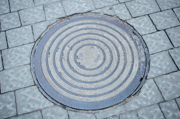 Fototapeta na wymiar Gray sewer hatch with pattern for drainage on the sidewalk