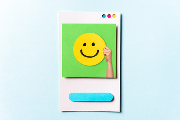 Concept of happy customer, employee, well done, feedback, opinion, social media. Hand showing a happy yellow smiling emoticon face on green and blue background with empty space for text.
