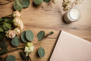 Beautiful flowers with the candle and notebook on the wood background. Holiday card. Holiday background. Planning holiday.