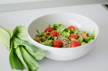 Bowl with salad and fresh vegetables on kitchen table. Healthy food