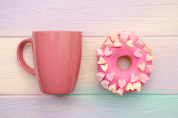 Sweet pink donut with icing and decoration with hearts on a rainbow background with a pink cup