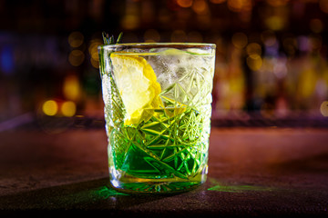 A green cocktail in an old fashion glass is on the bar