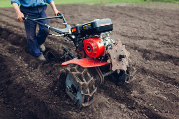 Farmer man driving small tractor for soil cultivation and potato planting. Spring agriculture preparation