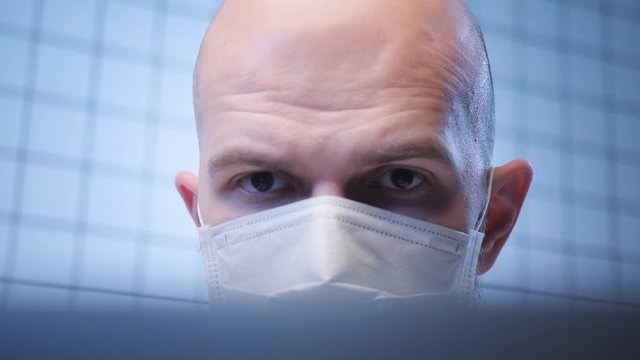 concentrated lab assistant in mask works on computer studying coronavirus infection in medical center closeup
