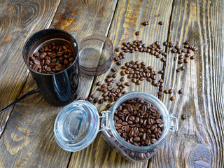 A coffee grinder with roasted coffee beans stands on a wooden table. coffee beans are scattered on the old wooden table top.