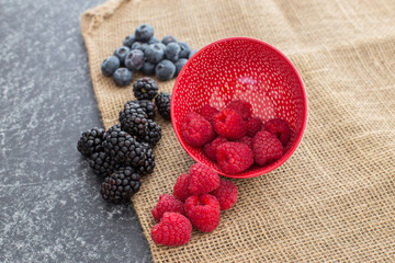 Mix of Red raspberries falling from a ceramic plate and a bunch of blackberries and blueberries in a rattan and black background. Stylish superfood photography