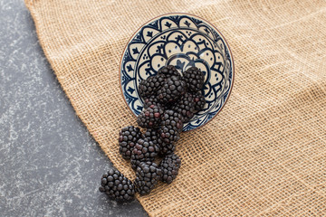Blackberries falling from a ceramic plate in a rattan and black background. Stylish superfood photography. Top View