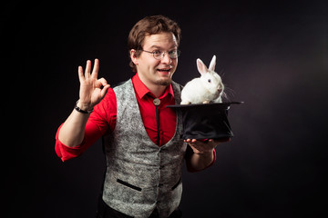 A magician is holding a cylinder hat with a white rabbit smiling. Focus miraculous appearance of...