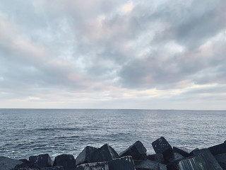 Soft focus image of seascape with square rocks and grey cloudy sky. 