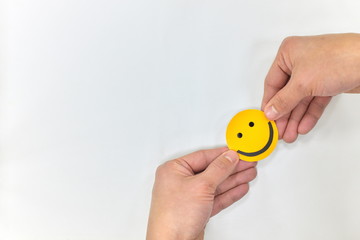 Hands holding a yellow smiley face on white background. Spread happiness concept.