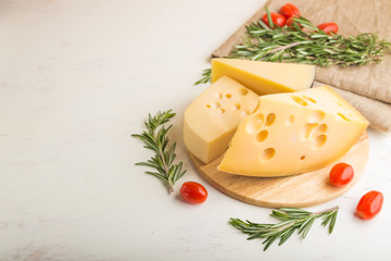 Various types of cheese with rosemary and tomatoes on wooden board on a white wooden background. Side view, copy space.