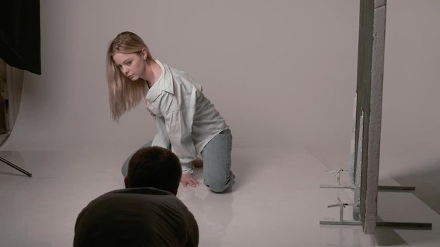 backstage of photographer taking pictures of sexy caucasian woman with long hair posing in beige lingerie, blue jeans on white studio floor. model tests of pretty girl in bra and shirt. photo shooting